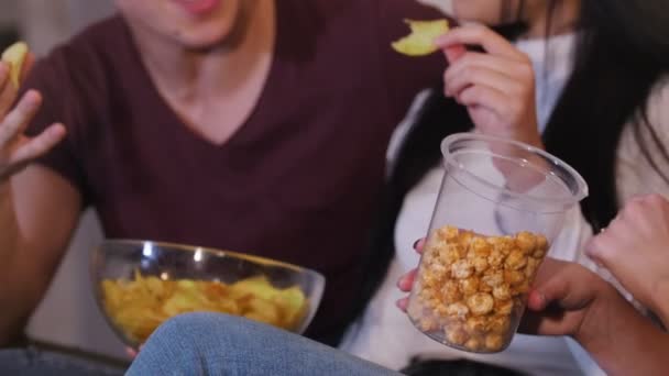 Compagnie de jeunes amis passant du temps ensemble. Regarder la télévision assis sur le canapé, parler et manger de la malbouffe 