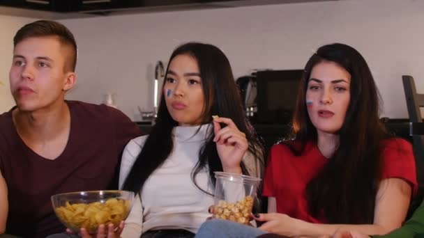 Compañía de jóvenes amigos que pasan tiempo juntos viendo televisión y comiendo palomitas de maíz y papas fritas — Vídeos de Stock