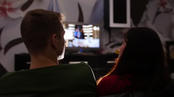 Joven linda pareja sentada en un sofá y viendo la televisión — Vídeo de stock