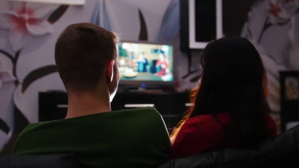 Jovem casal bonito sentado em um sofá, assistindo TV e abraços — Vídeo de Stock