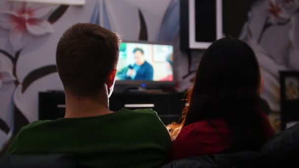 Jovem casal bonito sentado em um sofá e assistindo TV juntos — Vídeo de Stock