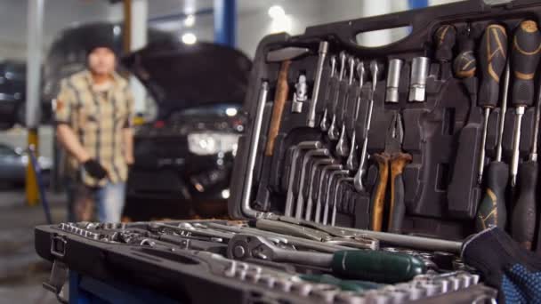 Autoservis. Mechanik muž chodí ke krytu Nástroj pro výběr správné velikosti klíč a odchází — Stock video