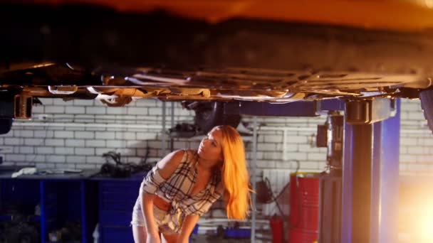 Bil reparationsservice. En bil hiss. Ung sexig kvinna som står under bilen. Löser problemet med en skiftnyckel — Stockvideo