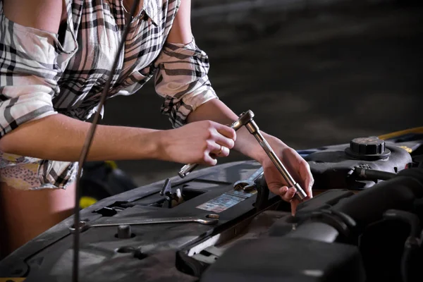 Auto reparatieservice. Jonge sexy vrouw staat voor een geopende auto kap en het werken met een moersleutel — Stockfoto