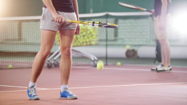 Тренировка на теннисном корте. Двое молодых людей бьют по мячу с пола. Ноги в фокусе — стоковое видео