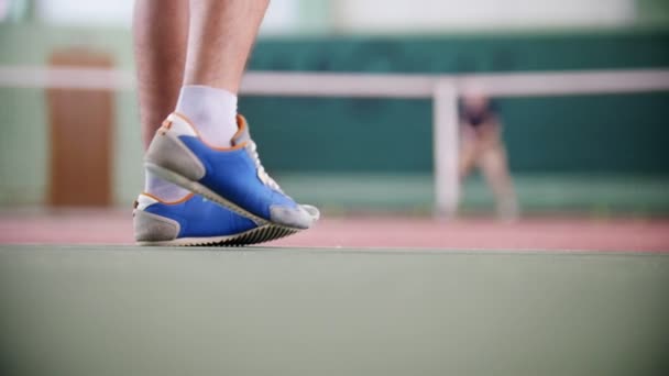 Entrenamiento en la cancha de tenis. Dos jóvenes jugando al tenis. Pies en botas azules en foco — Vídeo de stock