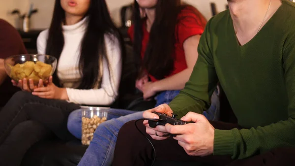 Três jovens sentados no sofá. Jovem segurando um joystick e mulheres segurando comida — Fotografia de Stock