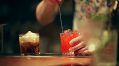 Barmen çalışıyor. Bir kaşık kullanarak cam bir alkollü kokteyl karışımı