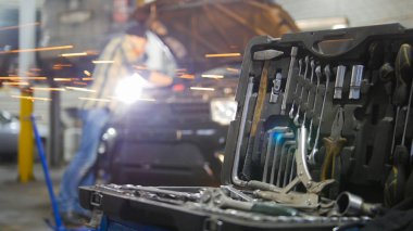Araba servisi. Açık kukuleta ile arabanın yanında duran ve bir araç ile çalışma mekanik adam. Toolcase üzerinde ön planda. Yangın parıldıyor