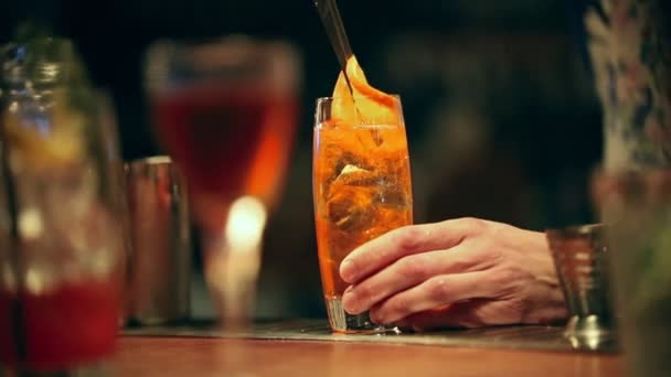 Camarero trabajando. Mezclando un cóctel alcohólico en el vaso. Añadir una rebanada de naranja — Vídeos de Stock