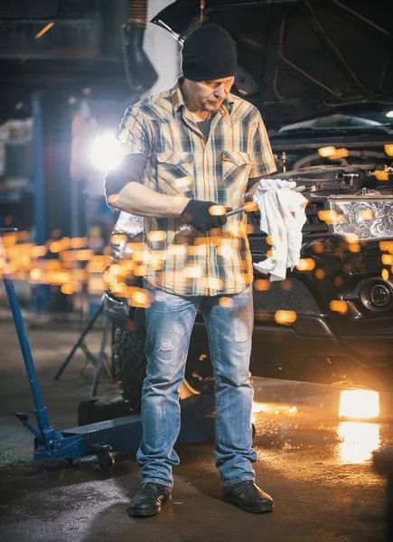 Servicio de coches. Hombre mecánico de pie junto al coche y limpia una herramienta con un trapo. Chispas — Foto de Stock