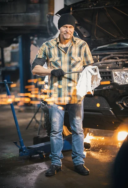 Servicio de coches. Hombre mecánico de pie junto al coche y limpia la herramienta, mirando en la cámara. Chispas — Foto de Stock
