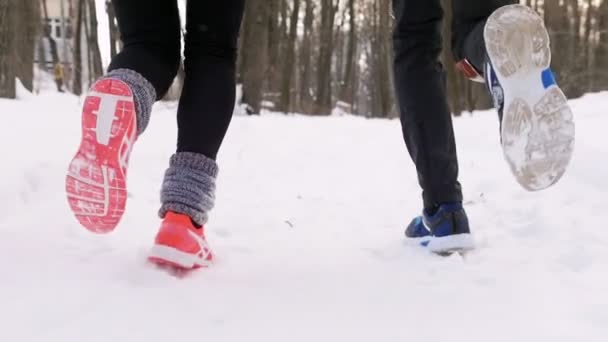 Foresta invernale. Giovane uomo e donna che fanno jogging. Piedi vista posteriore — Video Stock
