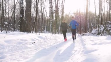 Kış orman. Sabah parkta iz üzerinde çalışan kadın ve genç erkek. Güzel güneş ışığı