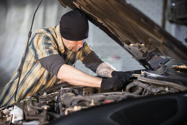 Autoservice. Brutale mechanic man die door de auto met open kap en controleert de status — Stockfoto