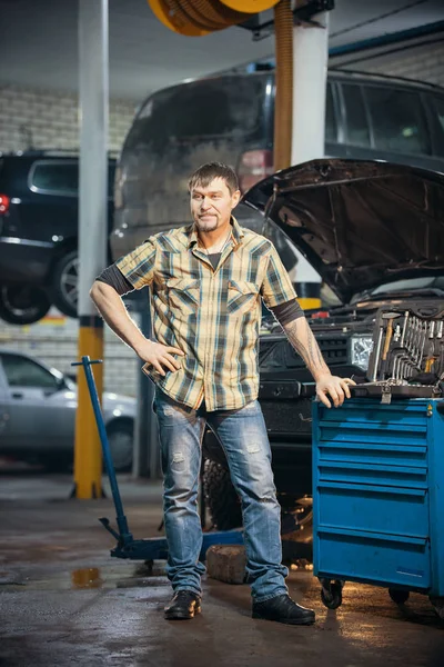Servicio de reparación de coches. Brutal hombre mecánico serio está al lado de la caja de herramientas — Foto de Stock