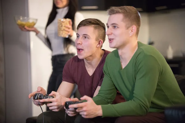 Companhia de jovens amigos que passam tempo juntos. Dois jovens jogando jogo enquanto suas namoradas trazem a comida — Fotografia de Stock