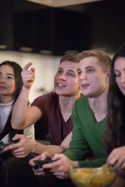 Jovens amigos sentados no sofá. Jovens segurando um joystick e mulheres comendo batatas fritas — Fotografia de Stock