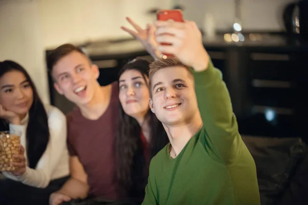 Jóvenes amigos sentados en el sofá y un joven tomando una selfie —  Fotos de Stock