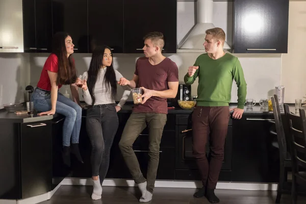 Four young people standing on kitchen and talking