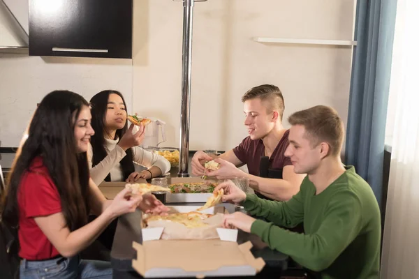 四个年轻朋友的公司坐在厨房里拿出比萨饼 — 图库照片