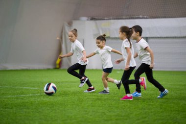 Çocuklar kapalı futbol oynuyor. Sahada topun peşinde koşuyoruz çocuklar