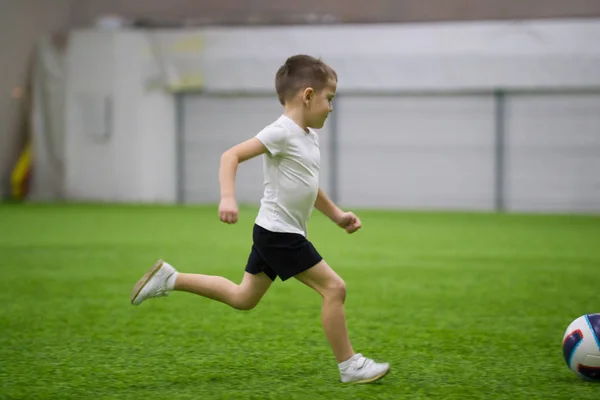 Играть в футбол в помещении. Маленький мальчик бежит по полю — стоковое фото