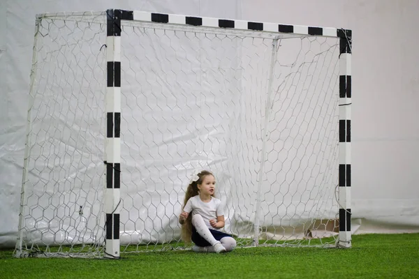 Kinder, die drinnen Fußball spielen. Ein kleines Mädchen sitzt im Fußballtor — Stockfoto