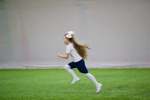 Παίζοντας ποδόσφαιρο σε εσωτερικούς χώρους. Ένα μικρό κορίτσι που τρέχει σε ένα ποδοσφαιρικό γήπεδο — Φωτογραφία Αρχείου
