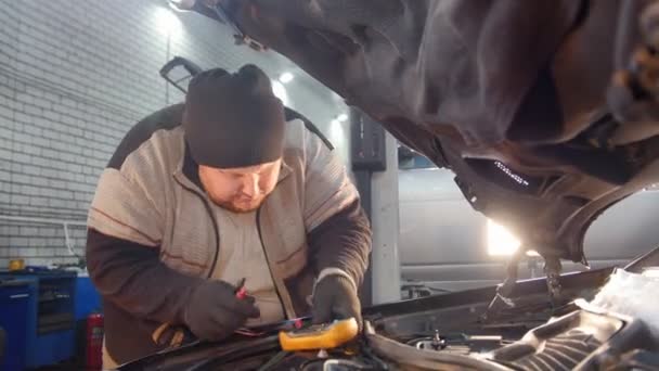 Autoservice. Dikke mechanic man controleert de spanning met een multimeter — Stockvideo