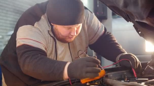 Autoservice. Dikke gember mechanic man controleert de spanning met een multimeter — Stockvideo