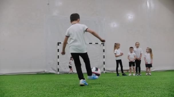 室内足球场。小孩子在踢足球。一个小男孩试图命中球门, 但女孩保护着大门 — 图库视频影像