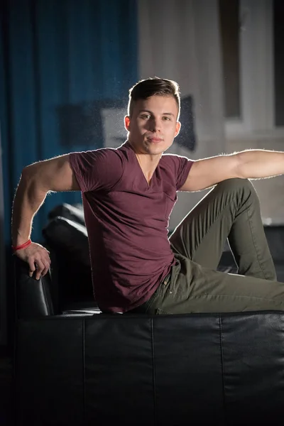 Young attractive fit guy posing for the camera. Sitting on a couch, looking in the camera