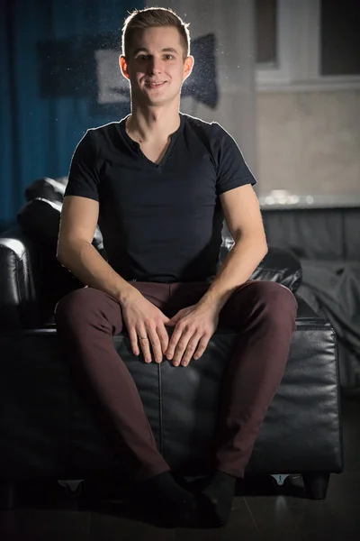 Ung attraktiv leende kille i mörk t-shirt som sitter på en soffa — Stockfoto