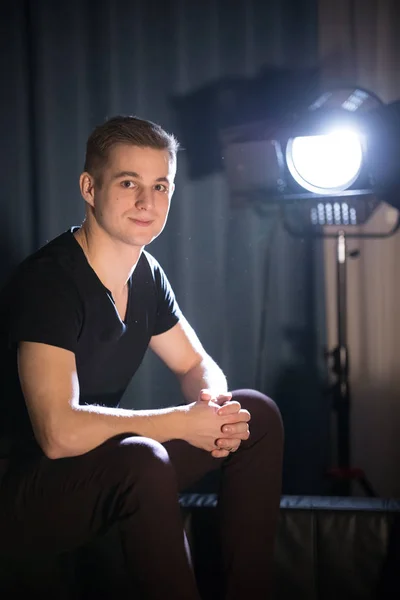 Jonge aantrekkelijke Glimlachende man in donkere t-shirt van de zittend op een bank en kijken in de camera. Poseren — Stockfoto