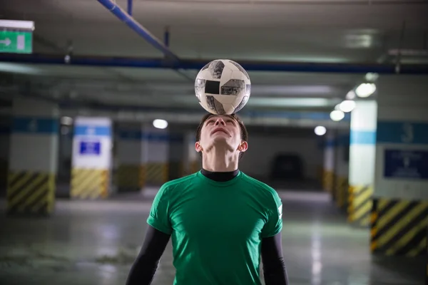 Football concept. Soccer player holding a ball on his head. Parking lot — Stock Photo, Image