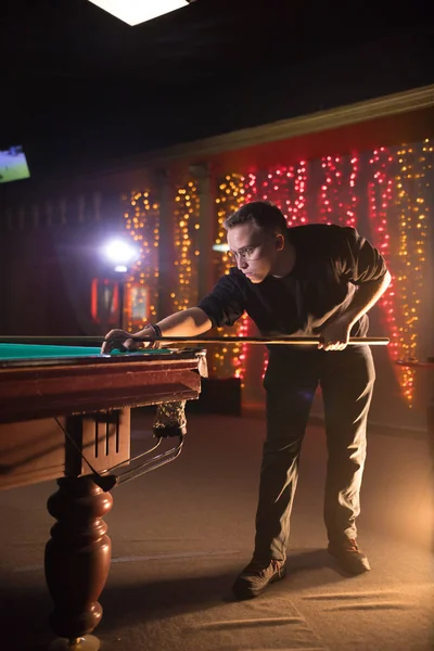 Entertainment concept. Young man in glasses playing billiard. Side view