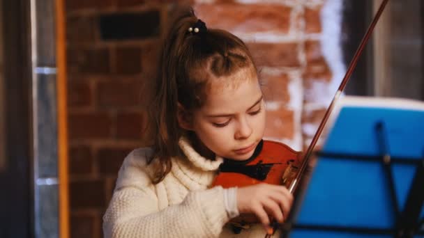 Маленька красива дівчинка в білому светрі грає на скрипці — стокове відео