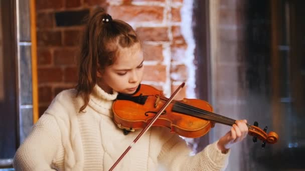Маленька дівчинка в білому светрі грає на скрипці — стокове відео