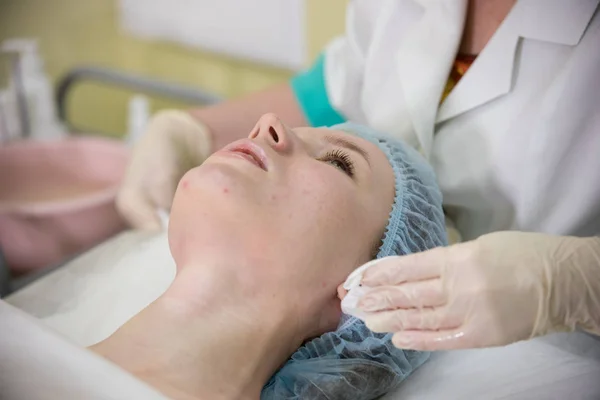 Clínica de Cosmetologia. Médicos mãos fazendo uma massagem facial para uma jovem deitada na cama, mulher conversando com o massagista — Fotografia de Stock