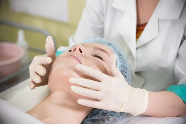 Primo piano delle mani dei medici che fanno un massaggio facciale a una giovane ragazza con gli occhi chiusi sdraiata a letto — Foto Stock