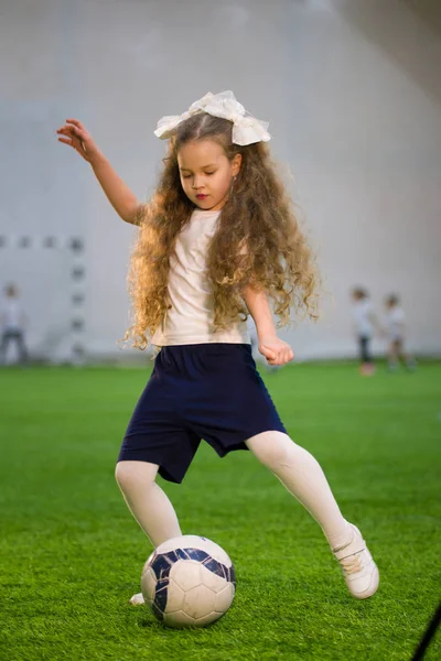 A little girl kicking the ball on the football field