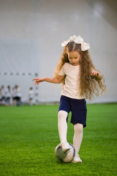 A little girl put her foot on the ball on the football field and ready to kick it