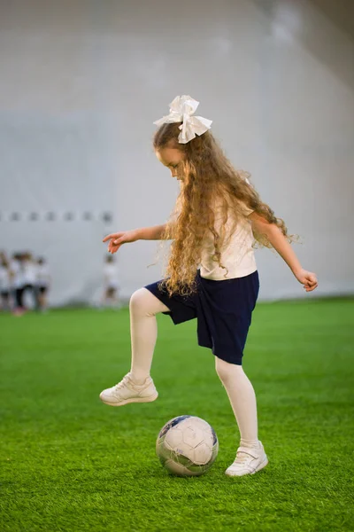 A little girl playing football holding your foot over the ball