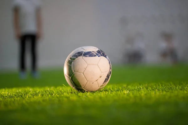 Weißer Ball auf dem grünen Rasen auf dem Fußballplatz und verschwommener kleiner Junge dahinter, waagerecht — Stockfoto