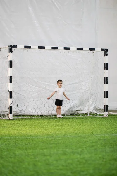 A little boy standing in the middle of a football goal on the field