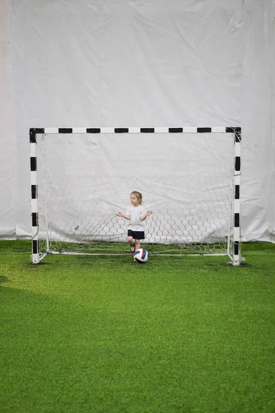Ein kleines Mädchen steht inmitten eines Fußballtores auf dem Feld — Stockfoto