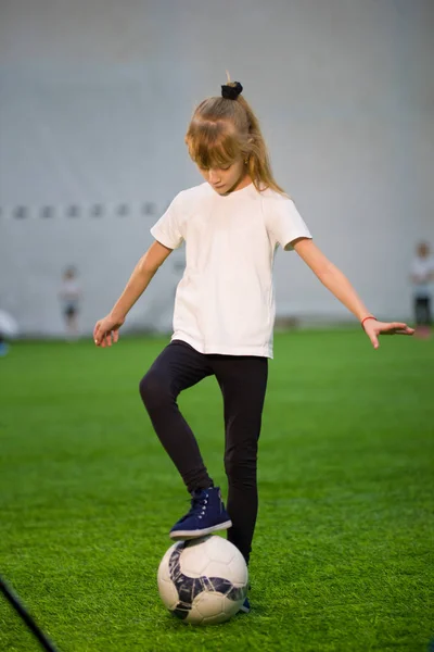 O fetiță și-a pus piciorul pe mingea de pe terenul de fotbal și s-a uitat la ea. — Fotografie, imagine de stoc