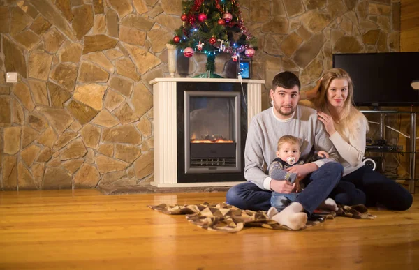Familia joven sentada en el suelo en una casa acogedora. Padres y un bebé — Foto de Stock