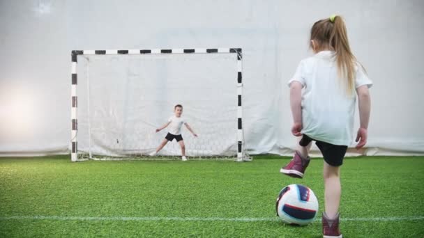 Niños jugando al fútbol. Una niña patea la pelota, pero el portero protege las puertas. — Vídeo de stock